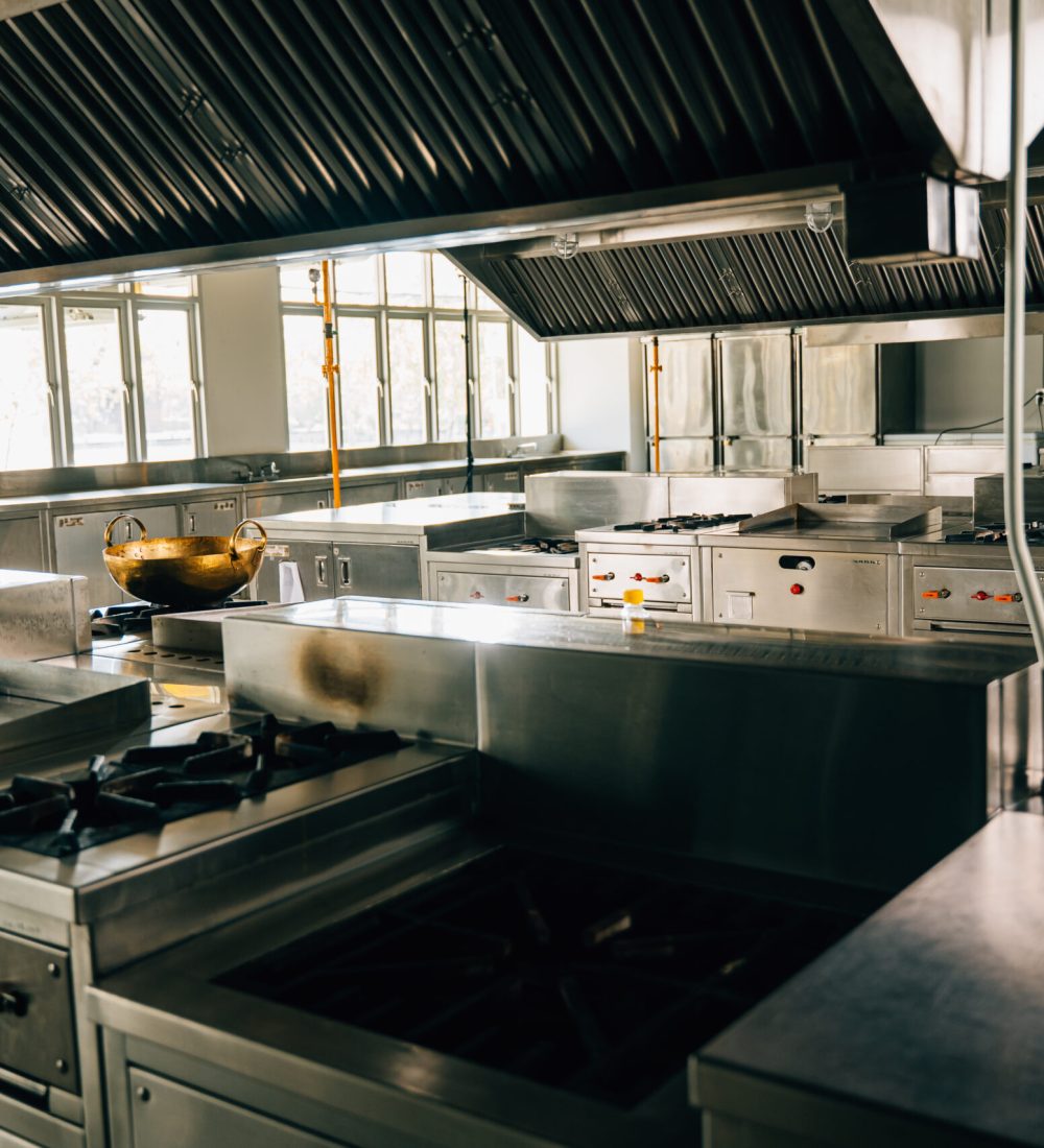 Professional kitchen in modern restaurant displays a shiny metal bowl on stove. Clean arrangement of equipment chrome appliances and new furniture. Bright gas service is working.